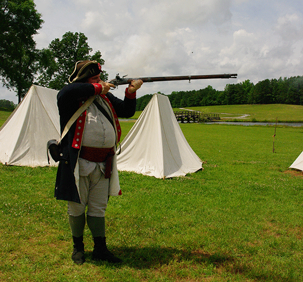 An interpreter prepares to fire his musket at the American Village. 