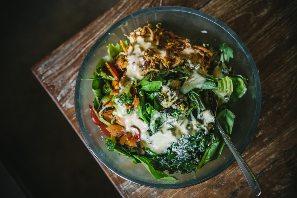 vegan-salad-with-various-veggies-and-greens-and-dressing-in-a-glass-bowl-on-a-wooden-table-closeup_t20_YwpEpW